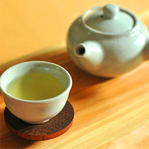 A cup of green tea next to a teapot